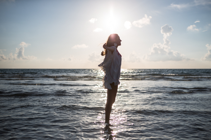 A person stands in shallow ocean water beneath a bright sky.