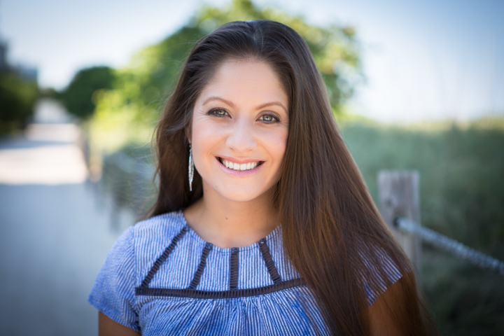 A smiling woman in a blue patterned top stands outdoors.