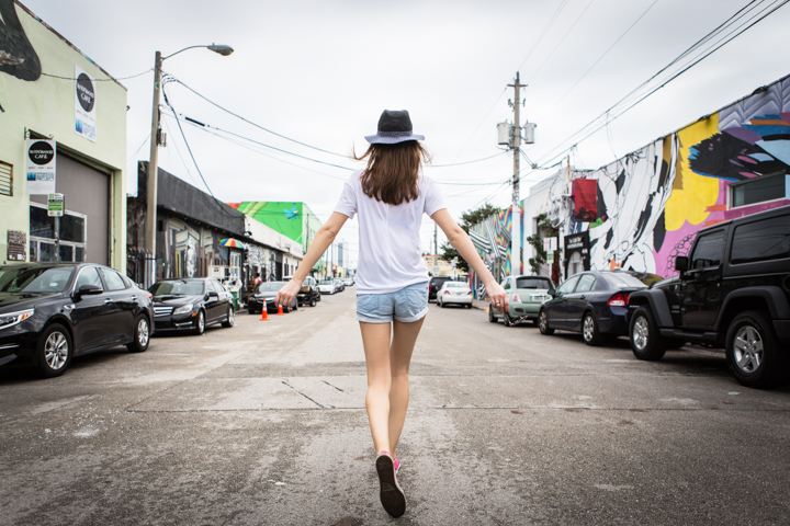 A woman in a hat walks down a street lined with colorful murals.