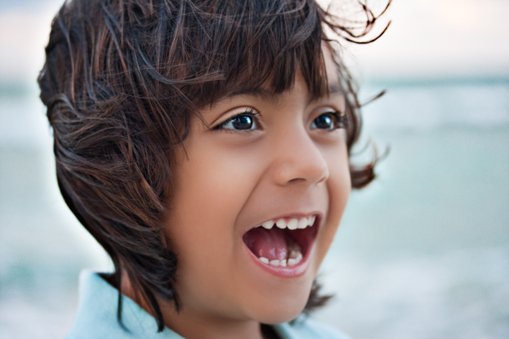 A laughing child with dark hair looks to the side outdoors.