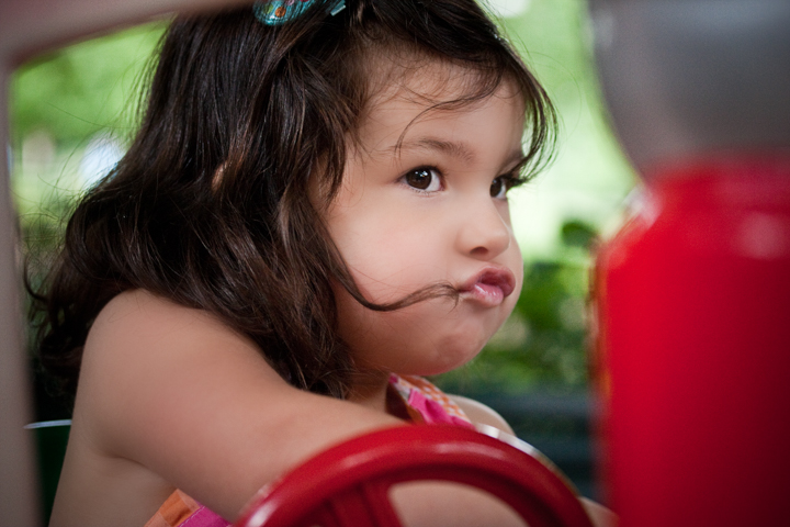 A toddler sits at a red playground steering wheel.