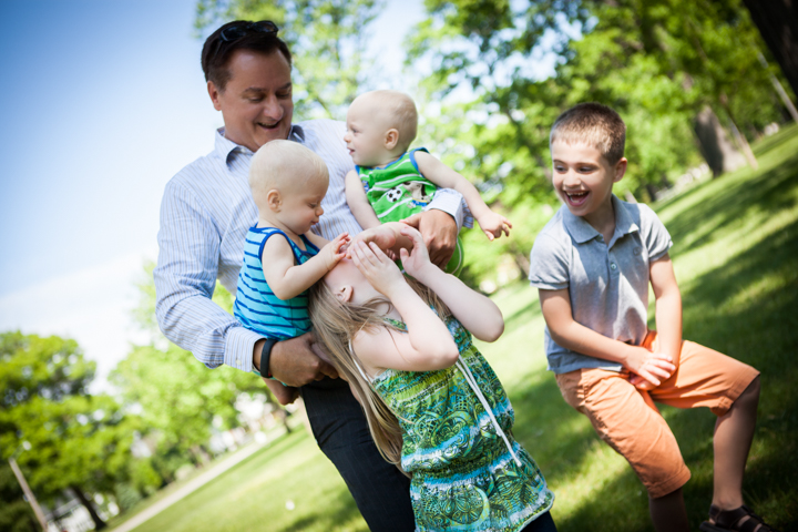 Two adults and two children stand together in a sunny green park.