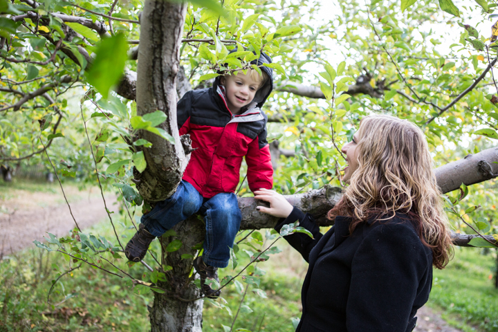A woman steadies a child sitting on a leafy tree branch.