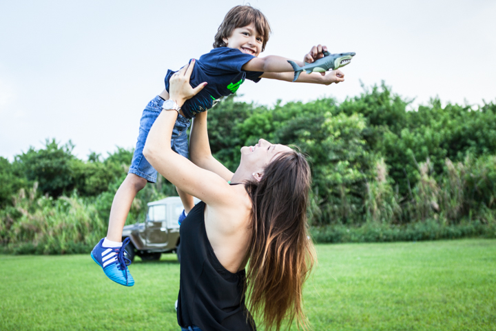 A woman lifts a laughing child into the air in a green field.