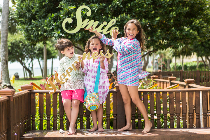 Three children in colorful outfits stand together on a wooden garden deck.