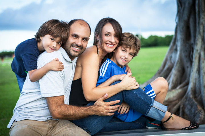 Two adults and two children cuddle together beside a garden tree.