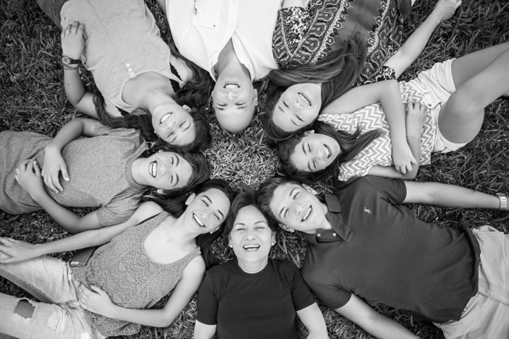 A group lies in a circle with their heads together in a black-and-white portrait.