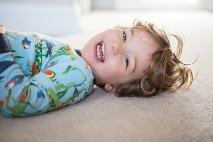 A laughing child lies on a carpet in colorful pajamas.