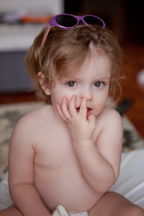 A toddler with sunglasses on their head rests a hand near their cheek.
