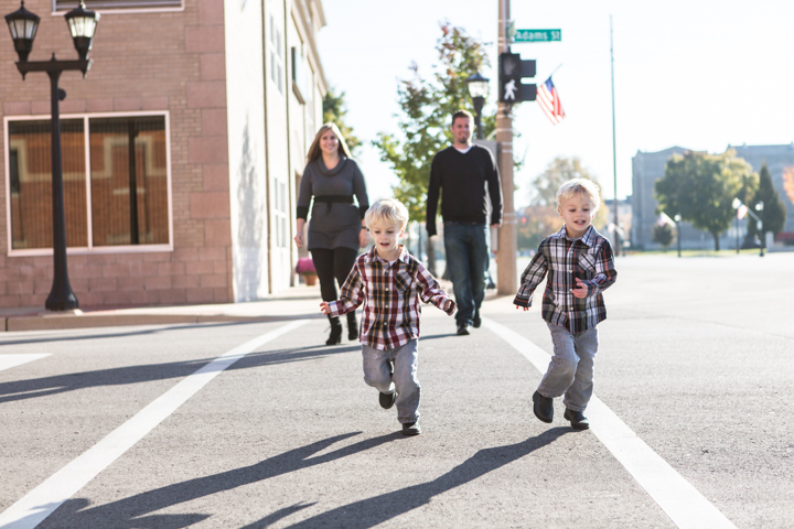Two children walk ahead of two adults across a sunny city street.