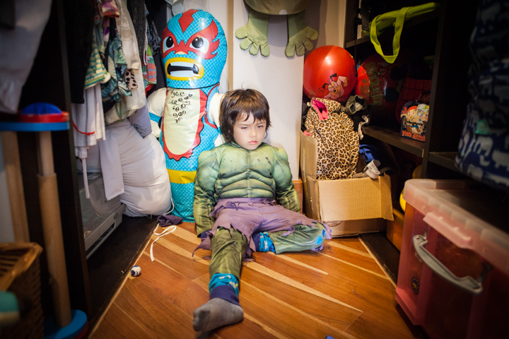 A child sits on a wooden floor among colorful toys and furniture.
