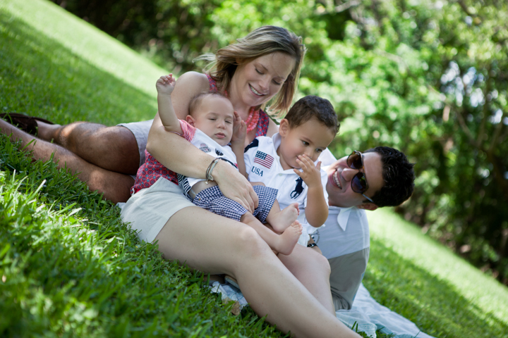 Two adults and two small children relax together on a grassy slope.