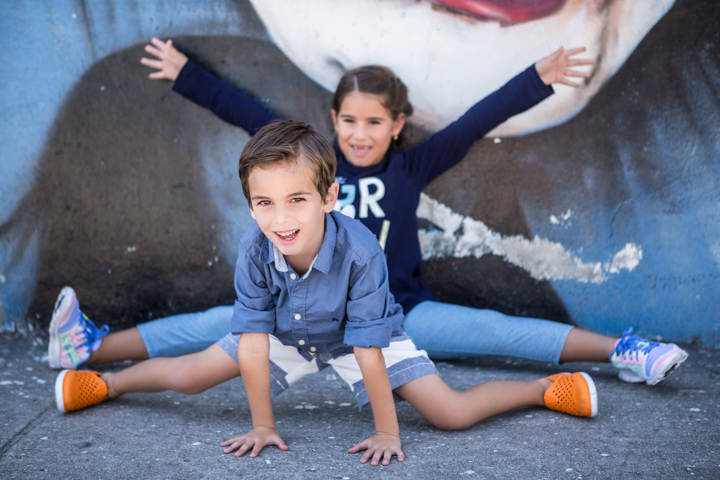 Two children stretch their legs and arms beside a painted wall.