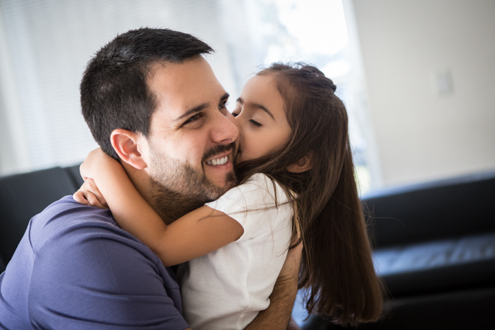 A child hugs a smiling man and kisses his cheek.