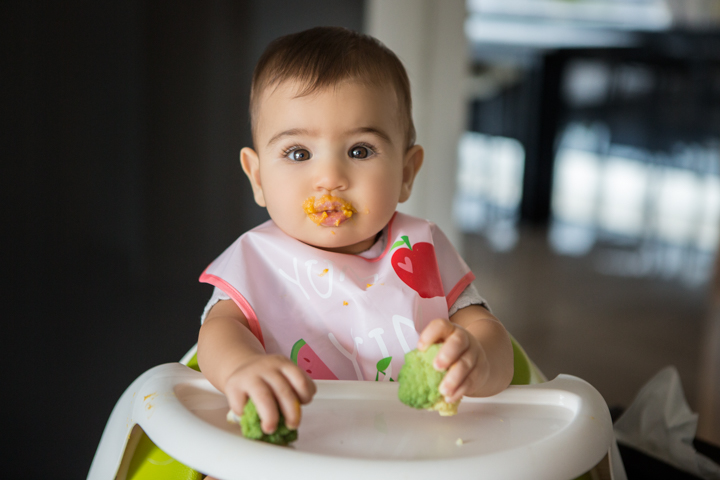 A toddler sits in a high chair with food around their mouth.