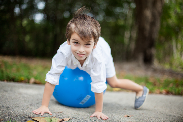 A smiling child balances over a blue ball on a garden path.