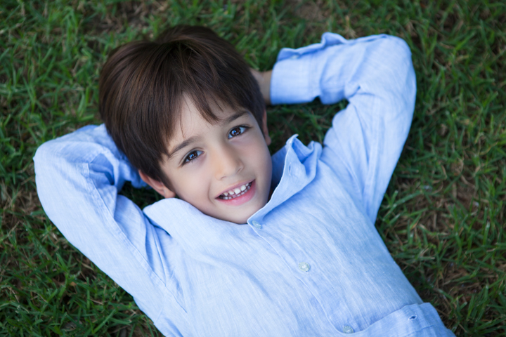 A child lies on the grass with both hands behind their head.