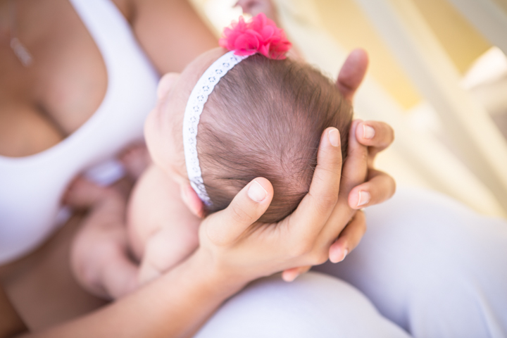 An adult gently cradles a baby's head beneath a pink flower headband.