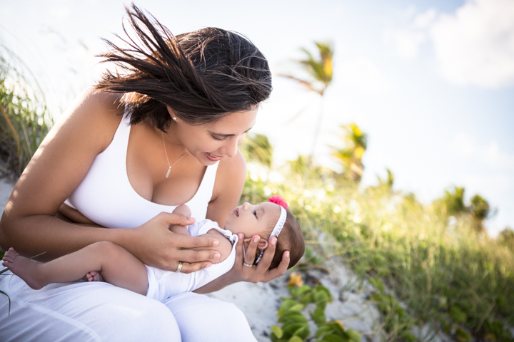 A woman looks down at a baby cradled in her arms on a sunny lawn.