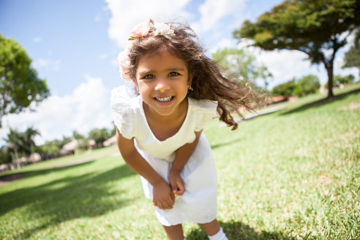 A smiling child leans toward the camera in a green park.