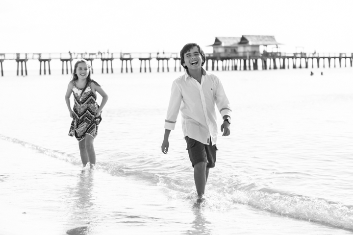 Two adults walk through shallow ocean water in a black-and-white photograph.