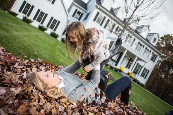A woman plays with a child in a pile of autumn leaves.
