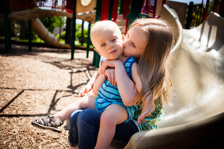 A child kisses a baby's cheek while holding them at a playground.