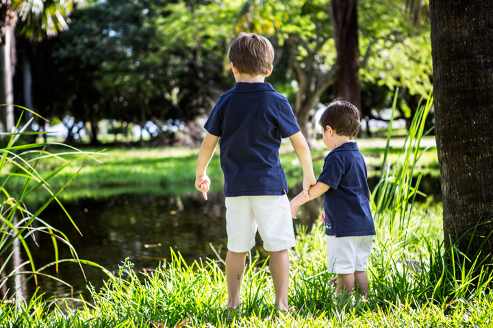 Two children stand hand in hand beside a garden pond.