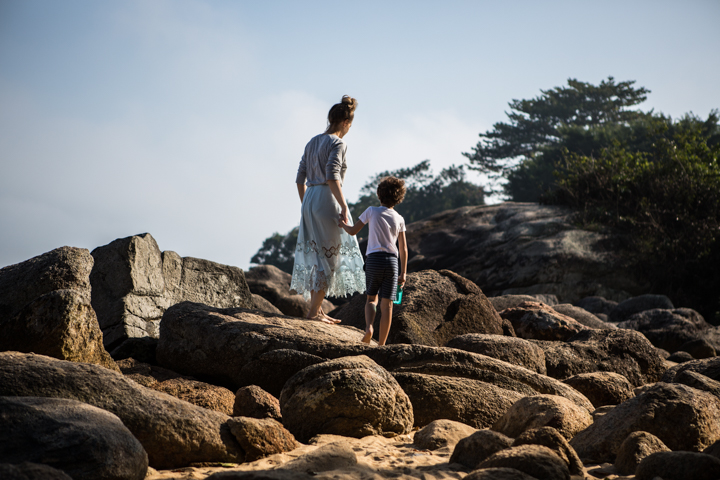 A woman and child stand together on large coastal rocks.