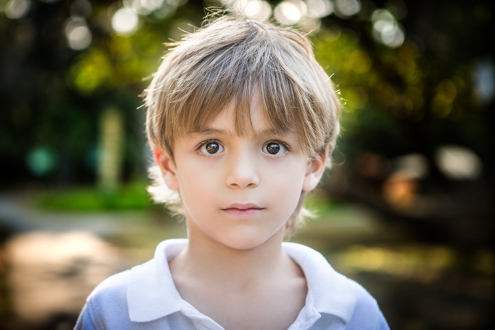 A child in a pale polo shirt looks toward the camera outdoors.