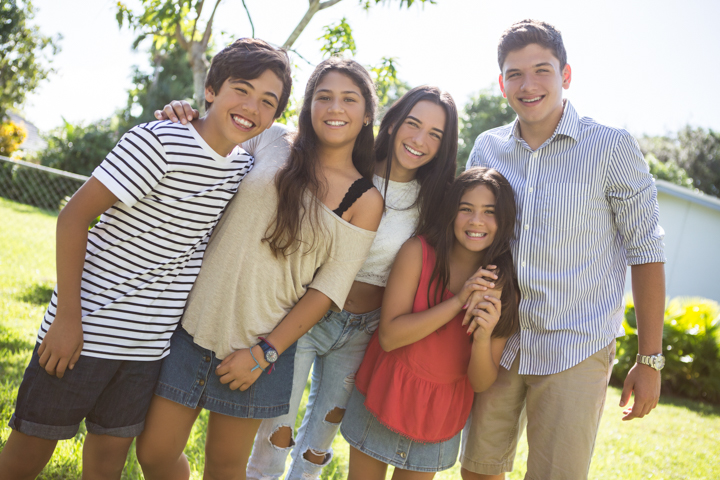 Two adults and three children lean together for an outdoor group portrait.