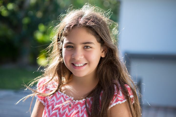 A smiling child in a pink patterned top stands outdoors.