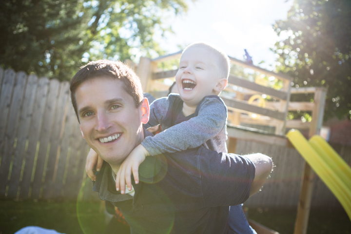 A laughing child rides on a smiling man's back at a playground.
