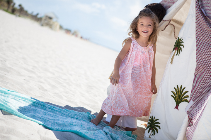 A smiling child in a pink dress stands beside a painted outdoor wall.