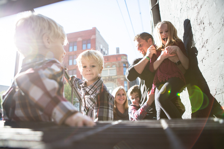 Adults and children gather around an outdoor table on a sunny city street.