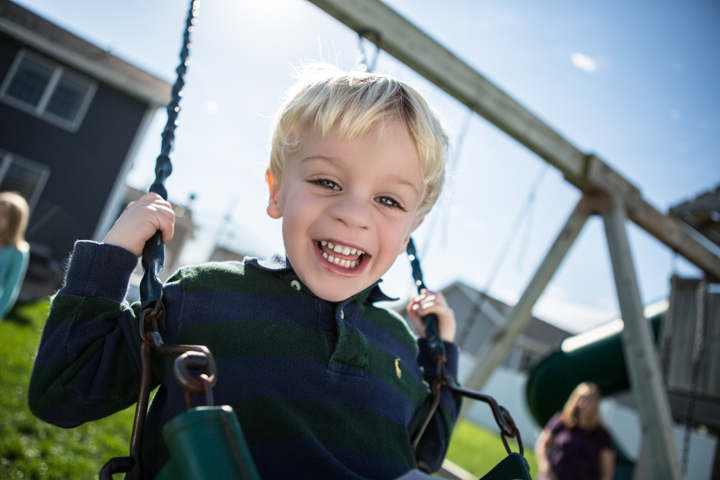 A laughing child holds the chains of a playground swing.