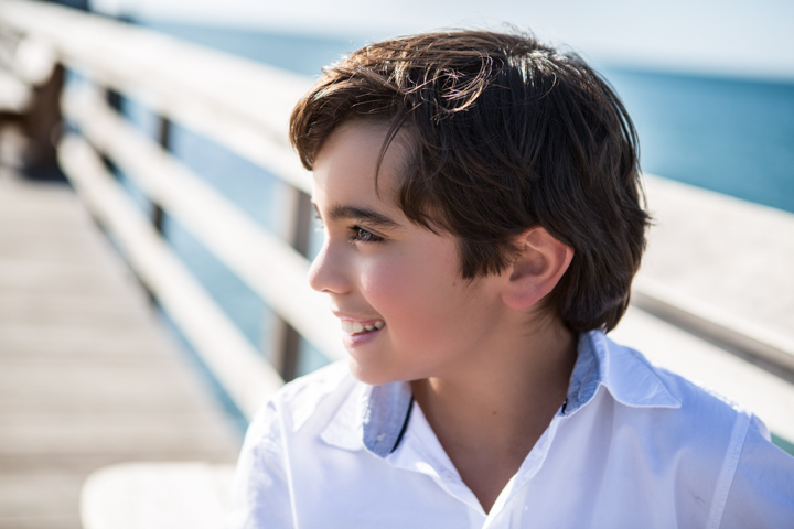 A child in a white shirt looks toward the water from a seaside walkway.
