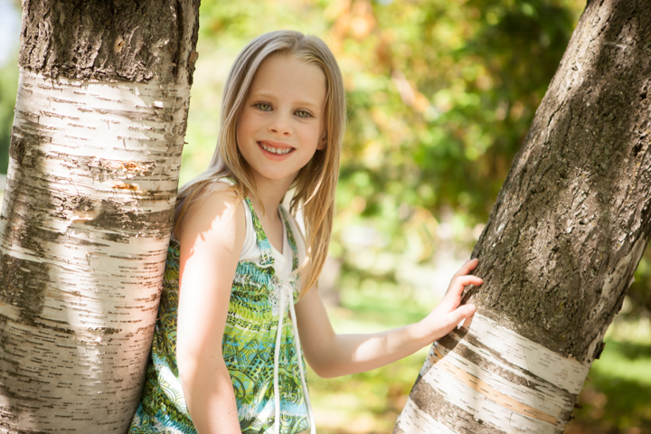 A smiling child stands between two garden tree trunks.