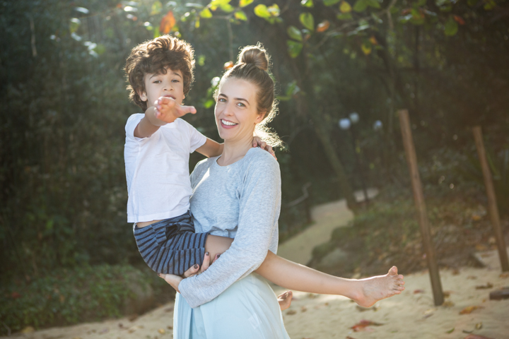 A smiling woman holds a child beside a garden swing.