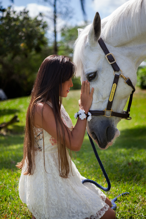 A woman in white sits beside a white horse in a green pasture.