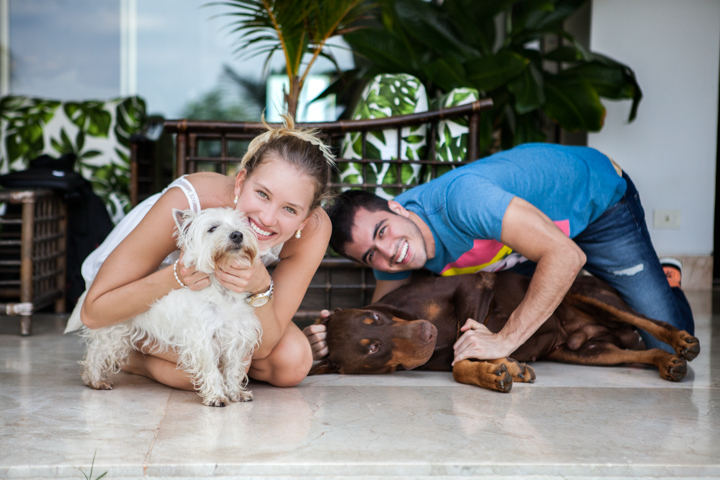 Two adults cuddle with two dogs on a tiled floor.