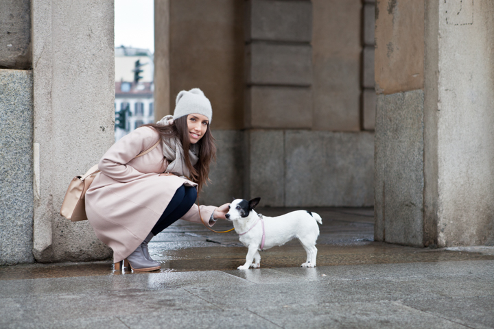 A woman in a pale coat crouches beside a small dog at a stone doorway.
