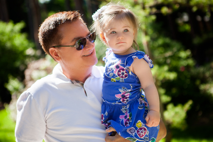 A man in sunglasses holds a young child on a sunny lawn.
