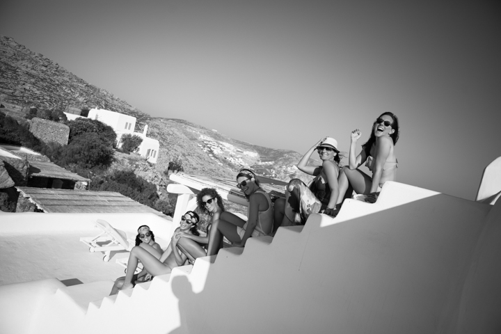 A group of women sits along white seaside steps in black and white.