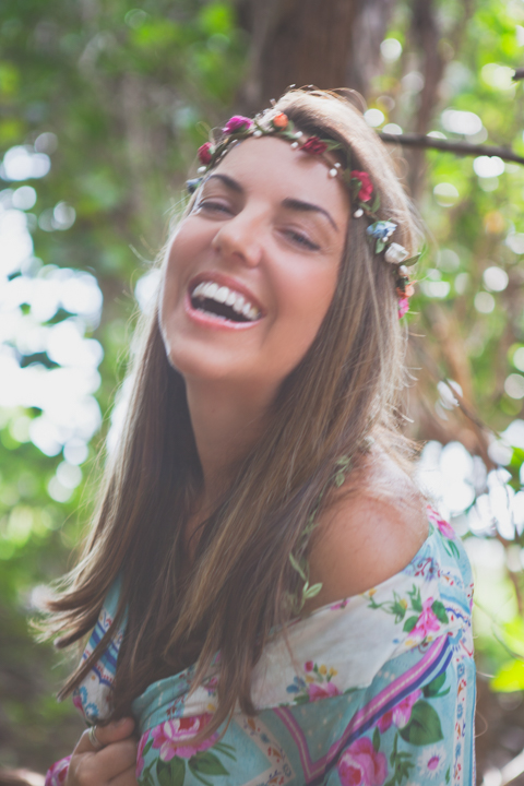A laughing woman wearing a flower crown stands outdoors.