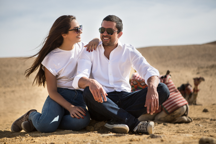 Two adults sit together on rocks in a sandy landscape.