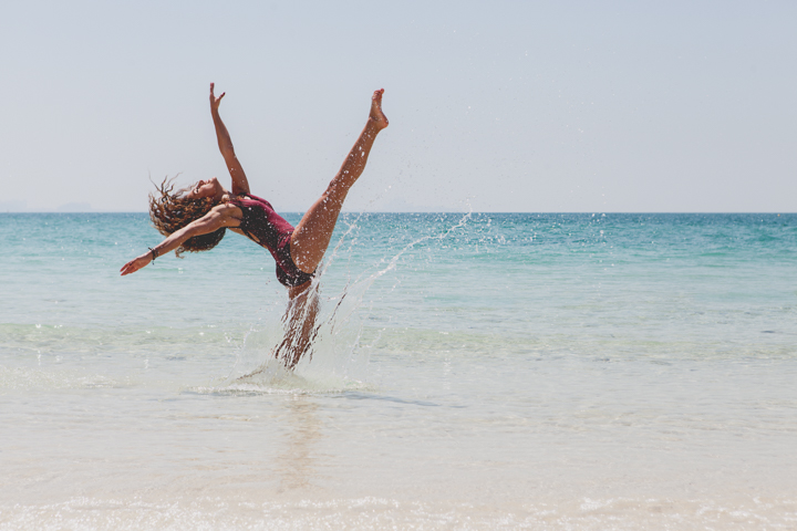 A person turns upside down in a playful jump at the edge of the sea.
