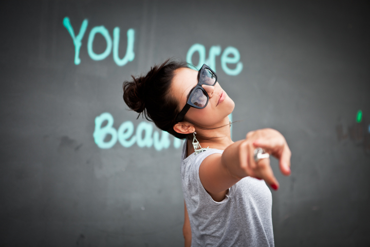 A man in sunglasses points toward the camera beside a painted wall.