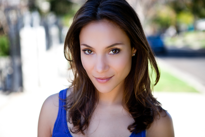 A woman in a blue sleeveless top looks toward the camera outdoors.