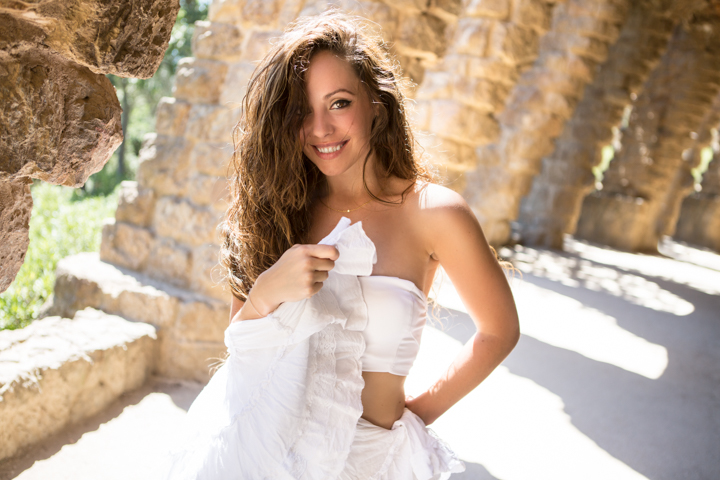 A smiling woman in white stands beside weathered stone walls.